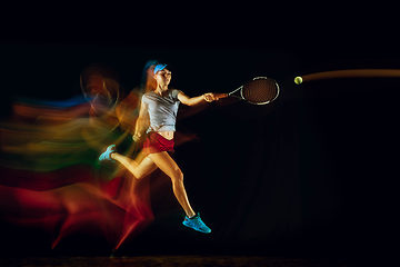 Image showing One caucasian woman playing tennis on black background in mixed light