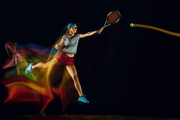 Image showing One caucasian woman playing tennis on black background in mixed light