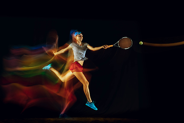 Image showing One caucasian woman playing tennis on black background in mixed light