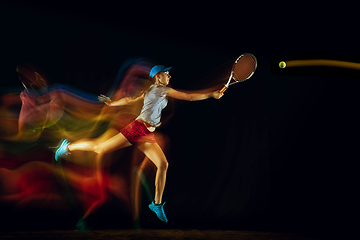 Image showing One caucasian woman playing tennis on black background in mixed light