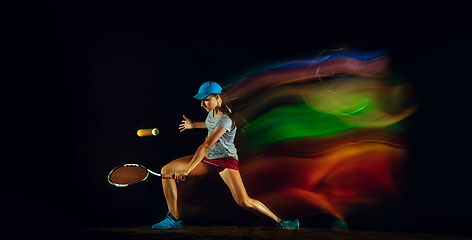 Image showing One caucasian woman playing tennis on black background in mixed light