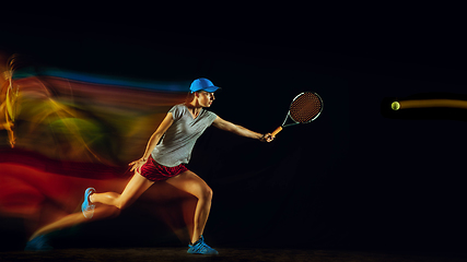 Image showing One caucasian woman playing tennis on black background in mixed light