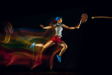 Image showing One caucasian woman playing tennis on black background in mixed light