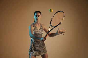 Image showing One caucasian woman playing tennis on brown background in mixed light