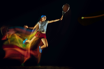 Image showing One caucasian woman playing tennis on black background in mixed light