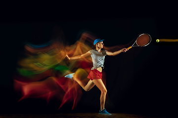 Image showing One caucasian woman playing tennis on black background in mixed light