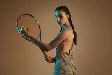 Image showing One caucasian woman playing tennis on brown background in mixed light