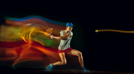 Image showing One caucasian woman playing tennis on black background in mixed light