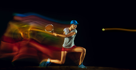 Image showing One caucasian woman playing tennis on black background in mixed light