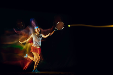 Image showing One caucasian woman playing tennis on black background in mixed light