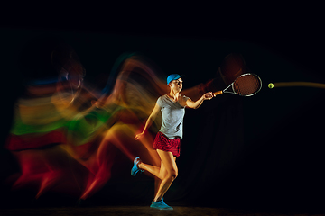 Image showing One caucasian woman playing tennis on black background in mixed light