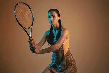 Image showing One caucasian woman playing tennis on brown background in mixed light