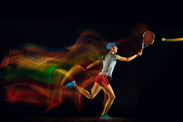 Image showing One caucasian woman playing tennis on black background in mixed light