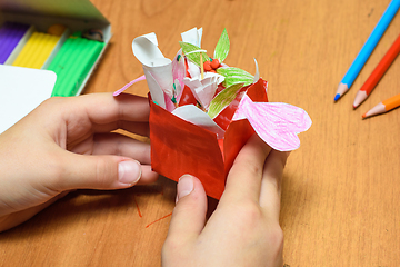 Image showing A girl holding a homemade gift for mom in her hands, stationery on the table in the background