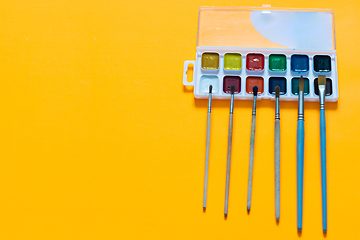 Image showing Watercolor paints and brushes of different sizes lie on an orange background