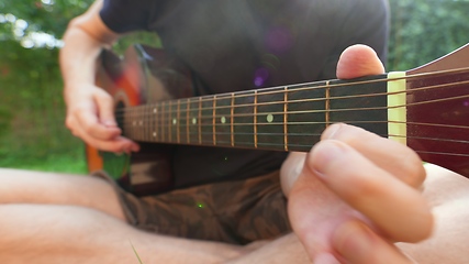 Image showing Man sitting in the grass playing guitar