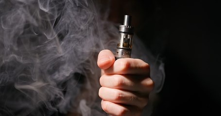 Image showing Electronic cigarette grabbed by male hand against dark background and vapor