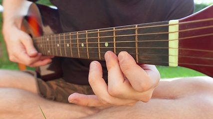 Image showing Man sitting in the grass playing guitar