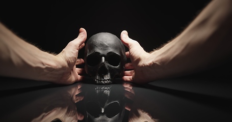 Image showing Hands reaching for black skull with reflection