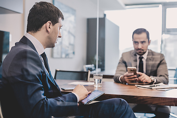 Image showing Two businessmen using smart phones and touchpad at meeting.