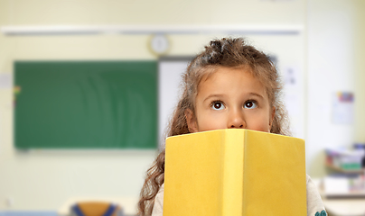 Image showing little girl hiding behind yellow book at school