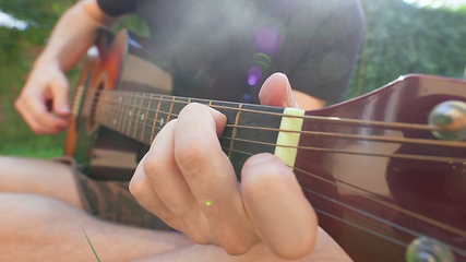 Image showing Man sitting in the grass playing guitar