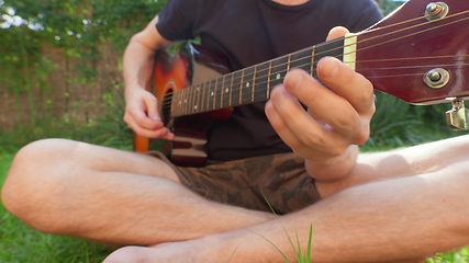 Image showing Man sitting in the grass playing guitar