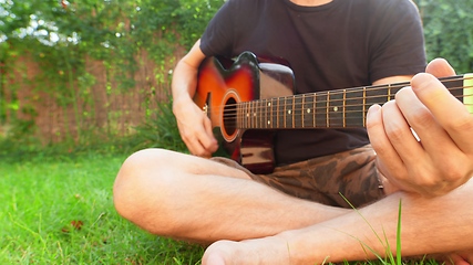 Image showing Man sitting in the grass playing guitar