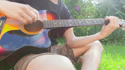 Image showing Man sitting in the grass playing guitar