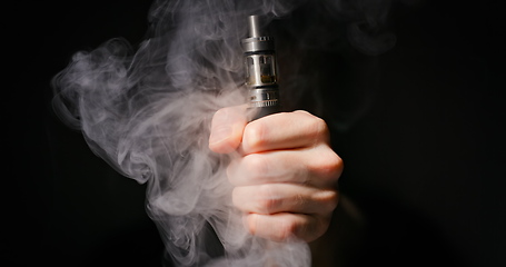 Image showing Electronic cigarette grabbed by male hand against dark background and vapor