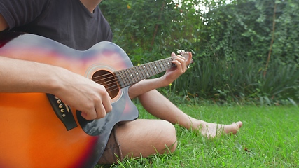 Image showing Man sitting in the grass playing guitar