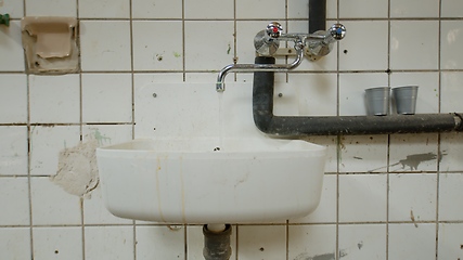 Image showing Old wash basin on tiled wall leaking water