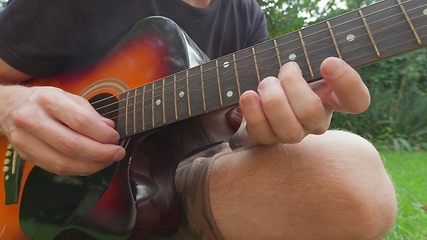 Image showing Man sitting in the grass playing guitar