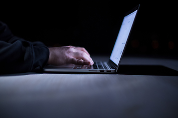 Image showing hacker using laptop computer while working in dark office