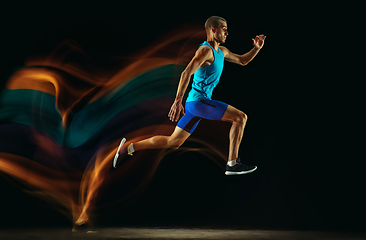 Image showing Professional male runner training isolated on black studio background in mixed light