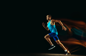 Image showing Professional male runner training isolated on black studio background in mixed light