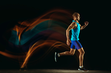 Image showing Professional male runner training isolated on black studio background in mixed light