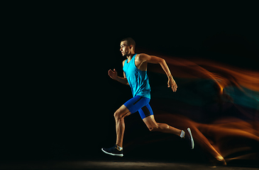 Image showing Professional male runner training isolated on black studio background in mixed light