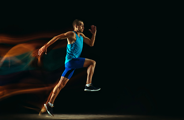 Image showing Professional male runner training isolated on black studio background in mixed light