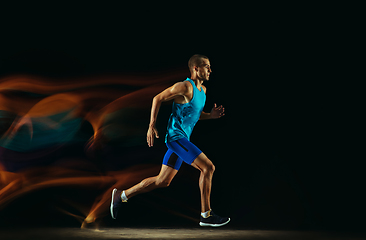 Image showing Professional male runner training isolated on black studio background in mixed light