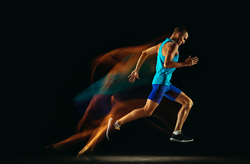 Image showing Professional male runner training isolated on black studio background in mixed light