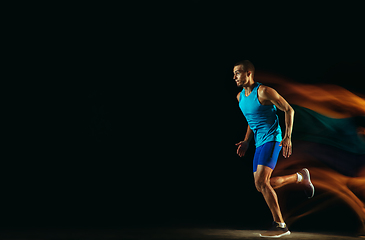 Image showing Professional male runner training isolated on black studio background in mixed light