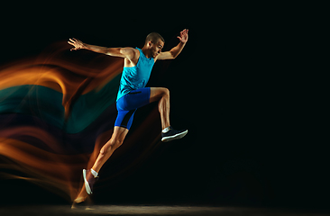 Image showing Professional male runner training isolated on black studio background in mixed light