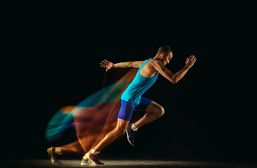 Image showing Professional male runner training isolated on black studio background in mixed light