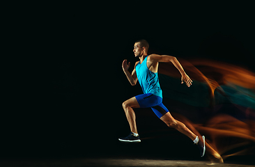 Image showing Professional male runner training isolated on black studio background in mixed light