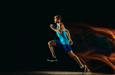 Image showing Professional male runner training isolated on black studio background in mixed light