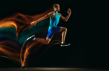 Image showing Professional male runner training isolated on black studio background in mixed light