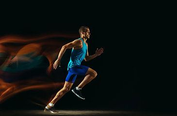 Image showing Professional male runner training isolated on black studio background in mixed light