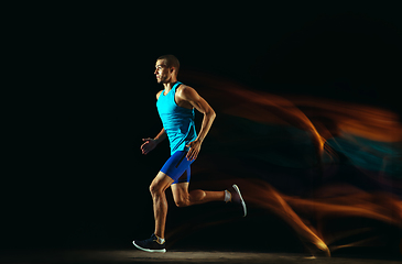 Image showing Professional male runner training isolated on black studio background in mixed light