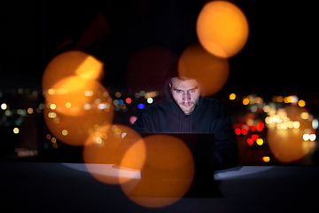 Image showing hacker using laptop computer while working in dark office